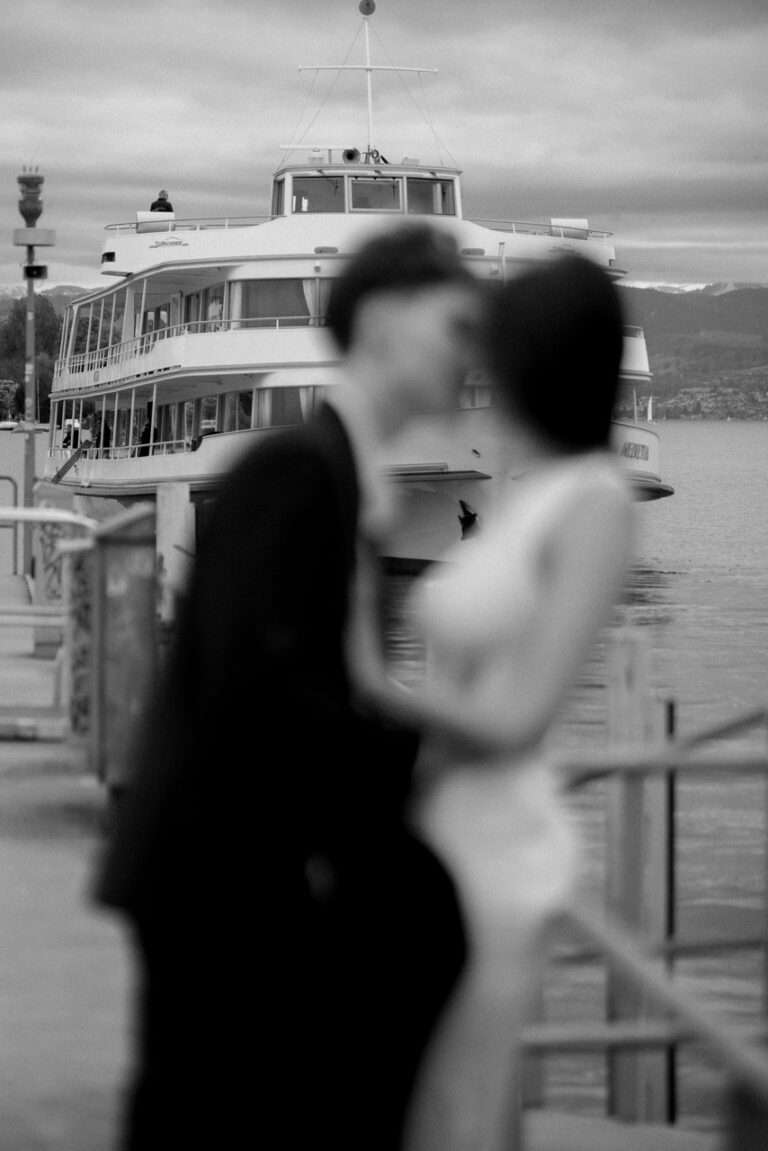 blurry black and white photo of a couple kissing each other with a boat behind them