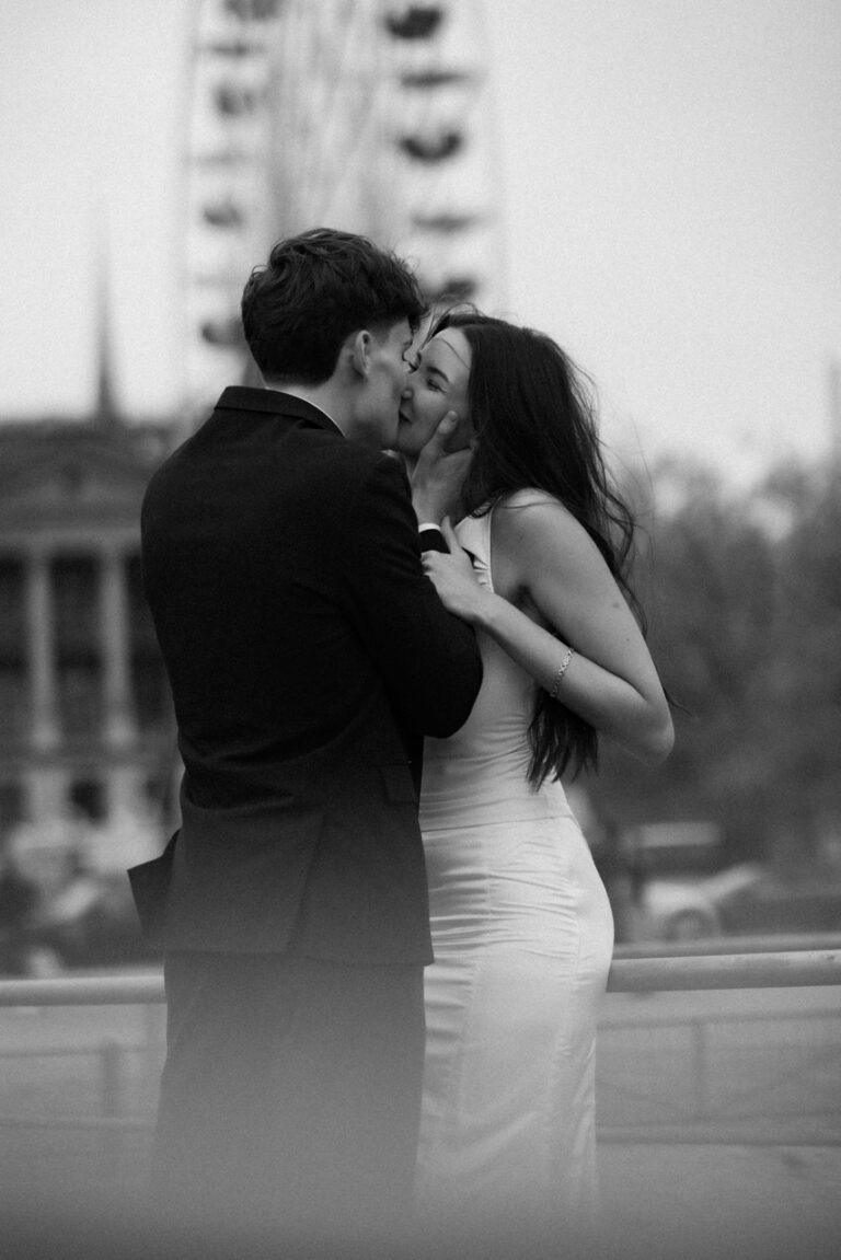 black and white photo of couple sharing a kiss with ferris wheel behind them